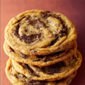 Pan-banging chocolate chip cookies on a cooling rack with melted chocolate chips